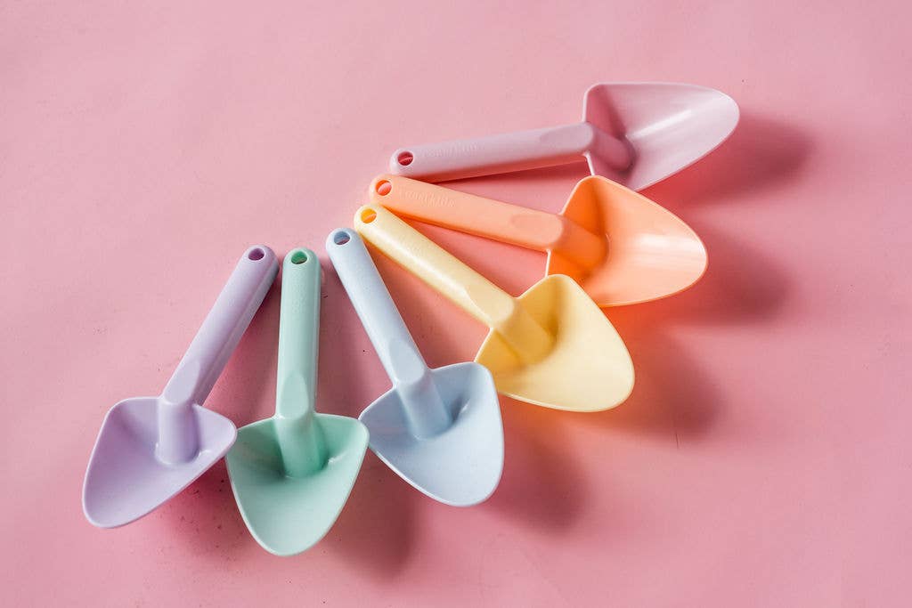 Set of colorful plastic shovels on a pink background